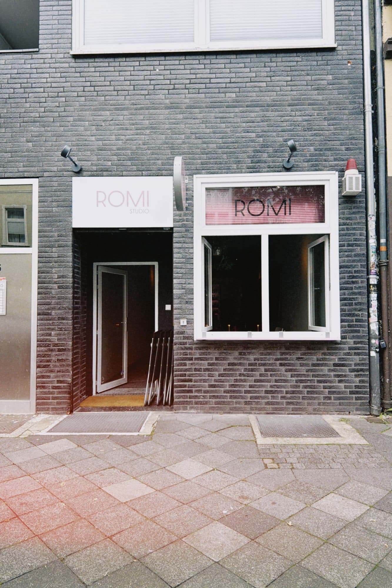 Die Fassade des ROMI Studio an der Hoffeldstraße in Düsseldorf-Flingern: graue Klinker, offene Tür, ROMI-Logo im Fenster